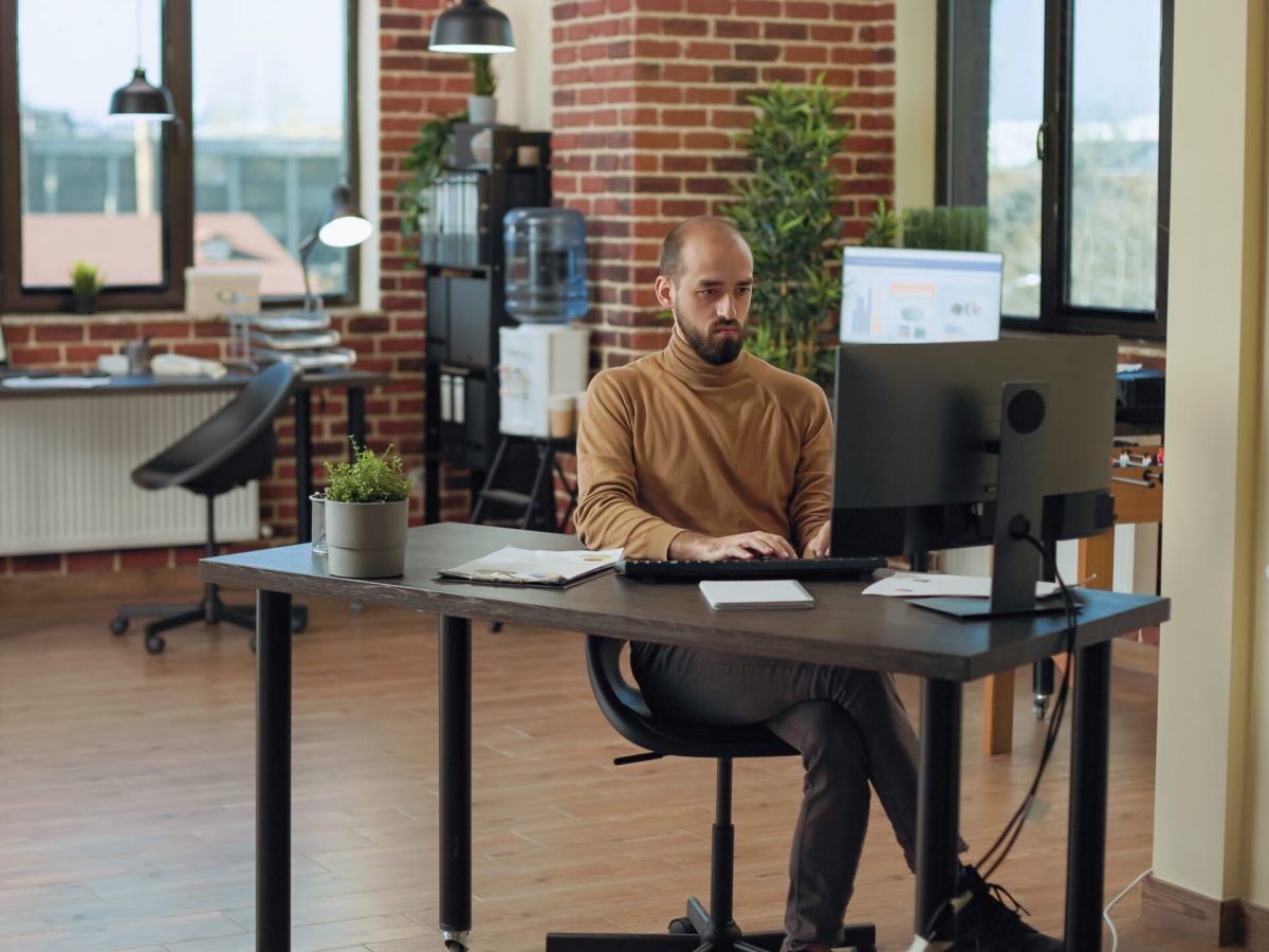 Company employee analyzing statistics and financial charts on computer and documents at desk. Male accountant doing management project task, planning network strategy and economy data.