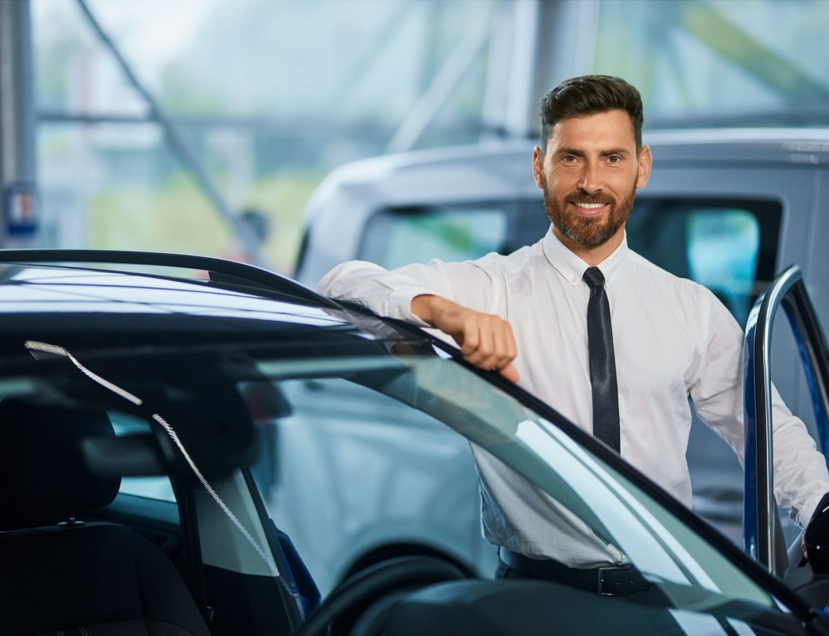 hombre-guapo-posando-cerca-de-un-coche-de-lujo-en-la-sala-de-exposicion